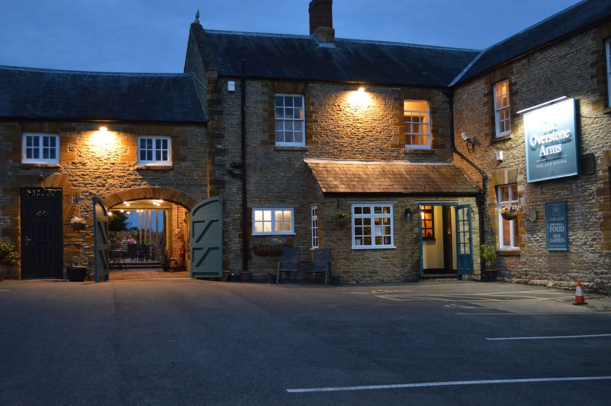 The Overstone Arms — warmly lit entrance at dusk, Stringers Hill, Pytchley